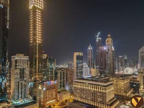 A nighttime cityscape with high-rise buildings, including a prominent tower with illuminated windows and a clock tower. - Vogue Park Tower DIFC  (Dubai)