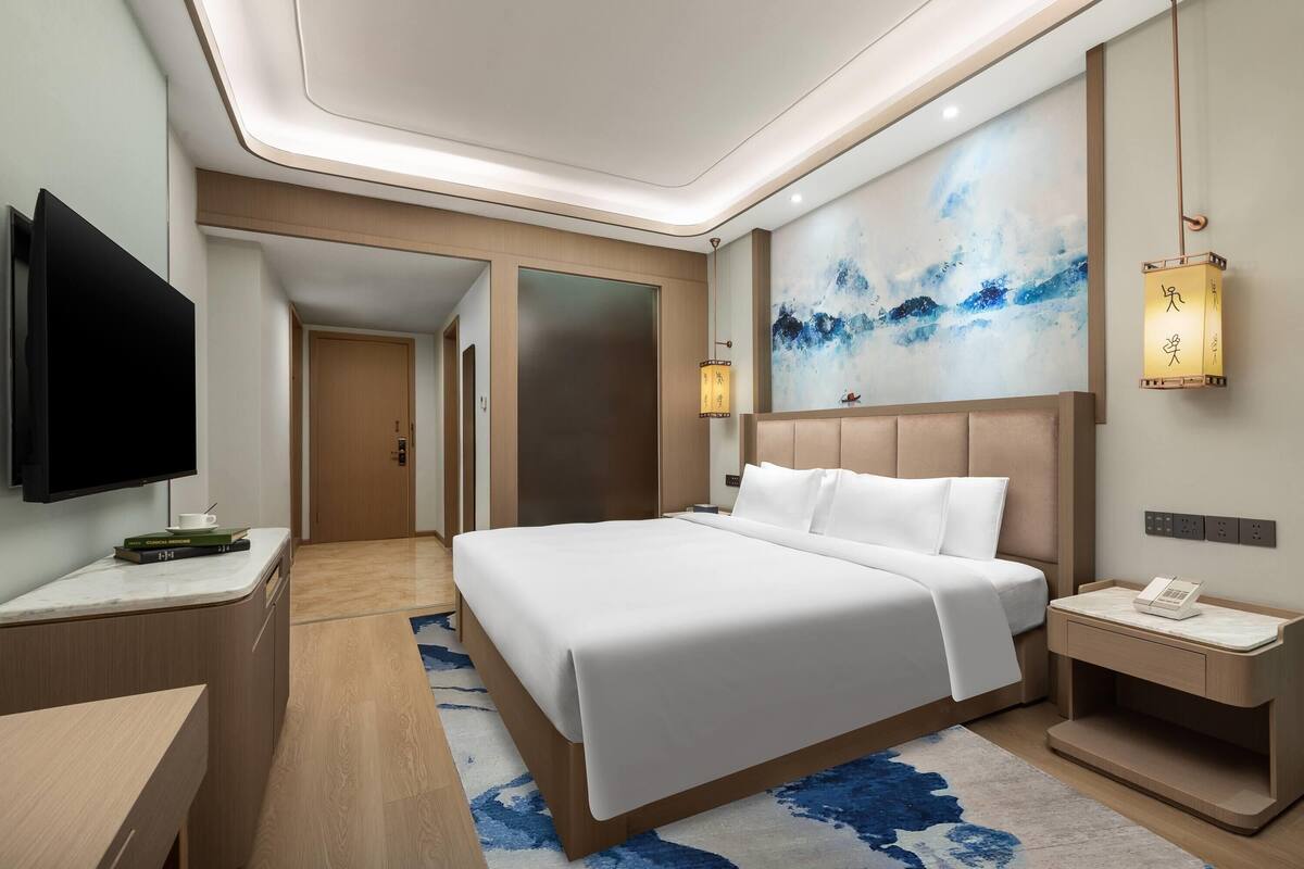 Una habitación de hotel moderna con una cama grande, un televisor de pantalla plana, un escritorio y una mesita de noche con teléfono.