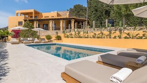 A pool area with lounge chairs and umbrellas, a building with a yellow facade, and a stone wall. - Villa Casa FOUR (Can Pep Simó)