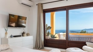 A bedroom with a large bed, a TV, a white dresser, and a balcony with a view of the sea. - Villa Casa FOUR (Can Pep Simó)