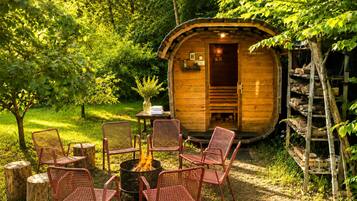 Une cabane en bois avec un foyer et des chaises, située dans un jardin luxuriant.