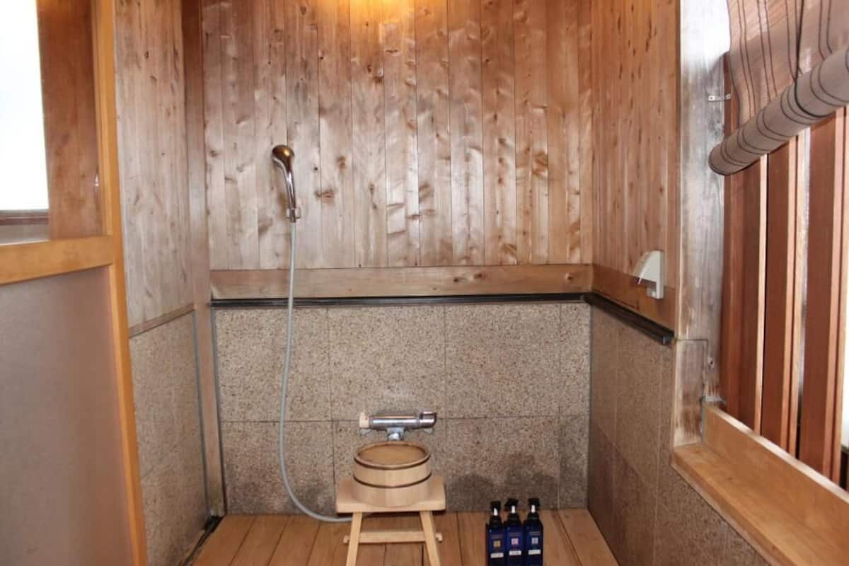 A sauna room with wooden walls, a wooden bench, a showerhead, and a set of bottles on the floor.