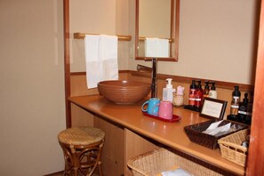 Un baño con tocador de madera, un lavabo grande, un espejo y un taburete de mimbre.