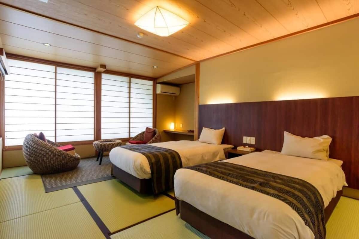 A traditional Japanese-style room with tatami flooring, two beds with dark headboards, and a shoji screen window.