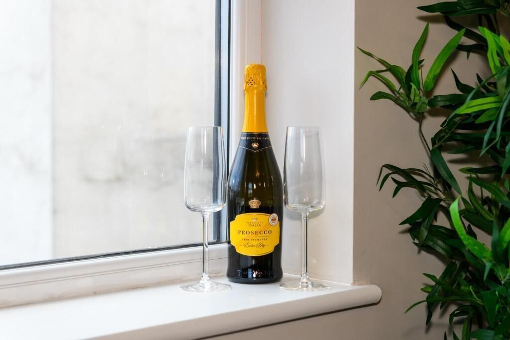 A bottle of Prosecco wine with two empty glasses on a windowsill.