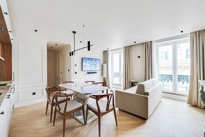 Ein modernes Wohnzimmer mit Essbereich, einer Couch und einem großen Fenster mit Vorhängen.