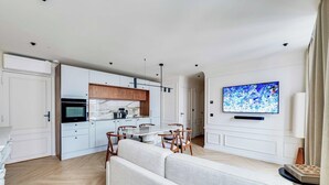 Un soggiorno moderno con divano, tavolo da pranzo e sedie, una cucina con mobili bianchi e un televisore a schermo piatto montato a parete.