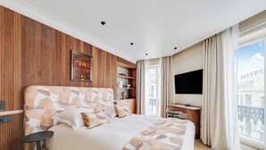 Una camera d'hotel moderna con un letto grande, una scrivania, una TV e un balcone con vista sulla città.