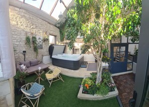 Un jardin intérieur accueillant, agrémenté d’un mur en pierre, d’un jacuzzi et de différents types de sièges.