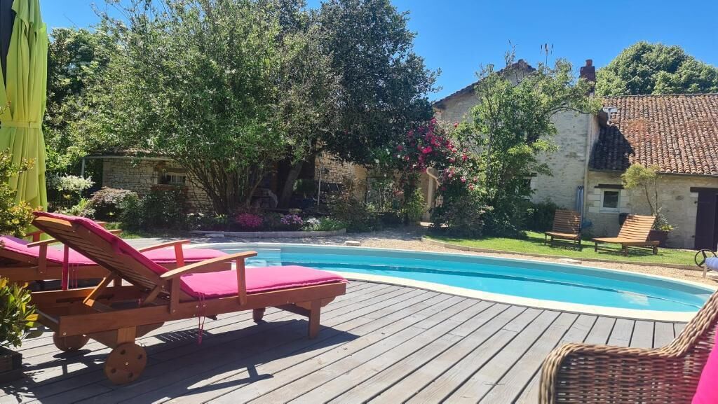 Une terrasse en bois avec une piscine, des chaises longues et un jardin agrémenté d’arbres et de fleurs.