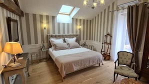 Un dormitorio con una cama grande, una mesita de noche, una lámpara, una silla y una ventana con cortinas.