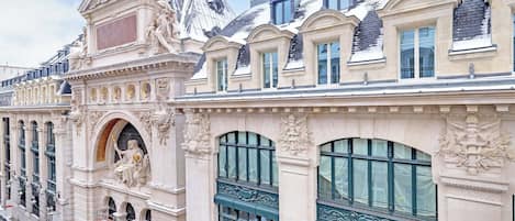 Un bâtiment historique doté de détails architecturaux raffinés, de grandes fenêtres et d’une statue sur la façade.