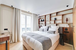 Un dormitorio con cama, mesitas de noche, estante de madera empotrado con objetos decorativos y vistas al exterior.