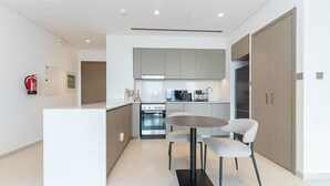 A modern kitchen with grey cabinets, a central island with chairs, a stove, and a fire extinguisher on the wall.