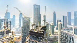 A high-rise building under construction with cranes, surrounded by other tall buildings.