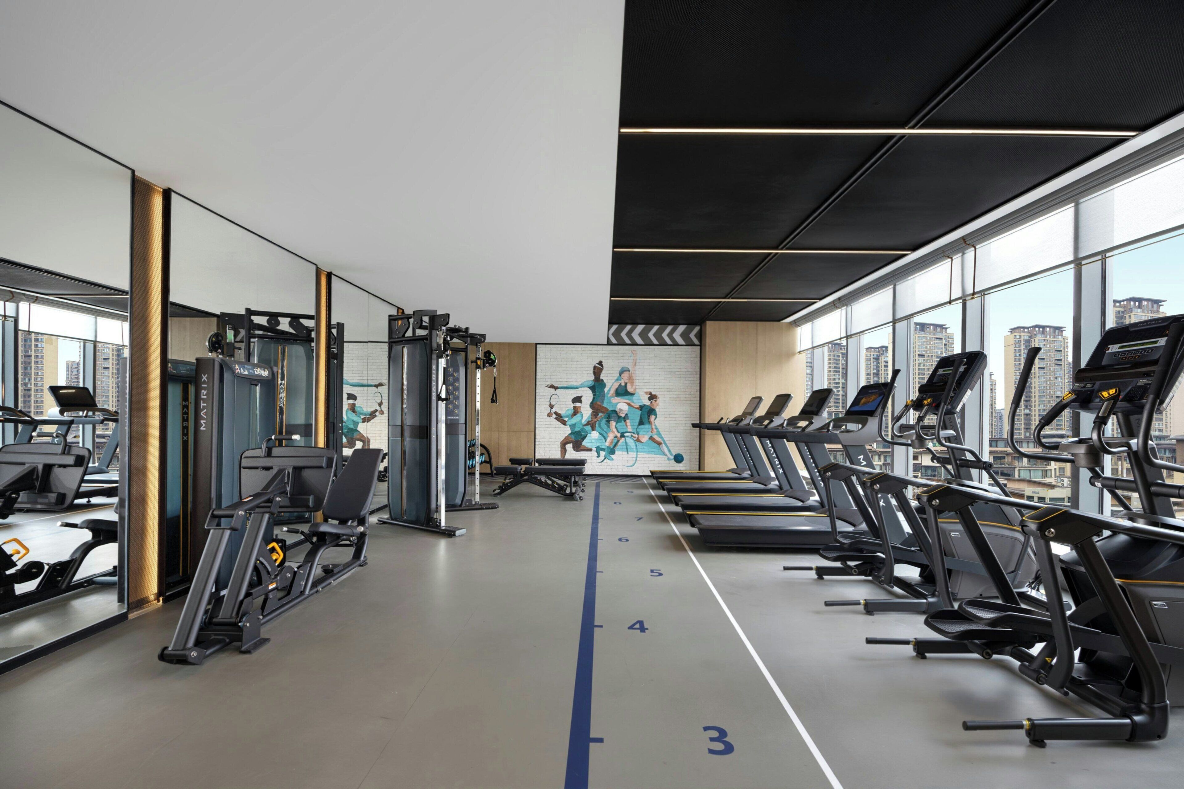 A gym with treadmills, weight machines, and a mural on the wall.
