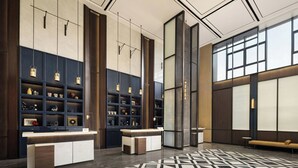 A modern lobby with a reception desk, shelving with decorative items, a patterned floor, and large windows. - Four Points by Sheraton Hanzhong Riverside (Hanzhong)