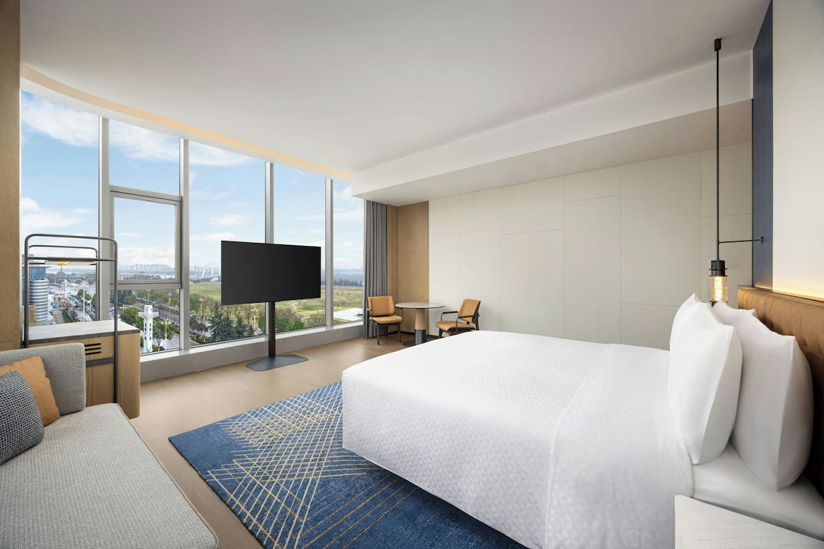 A hotel room with a large bed, a TV, a sofa, a small table, and a chair.