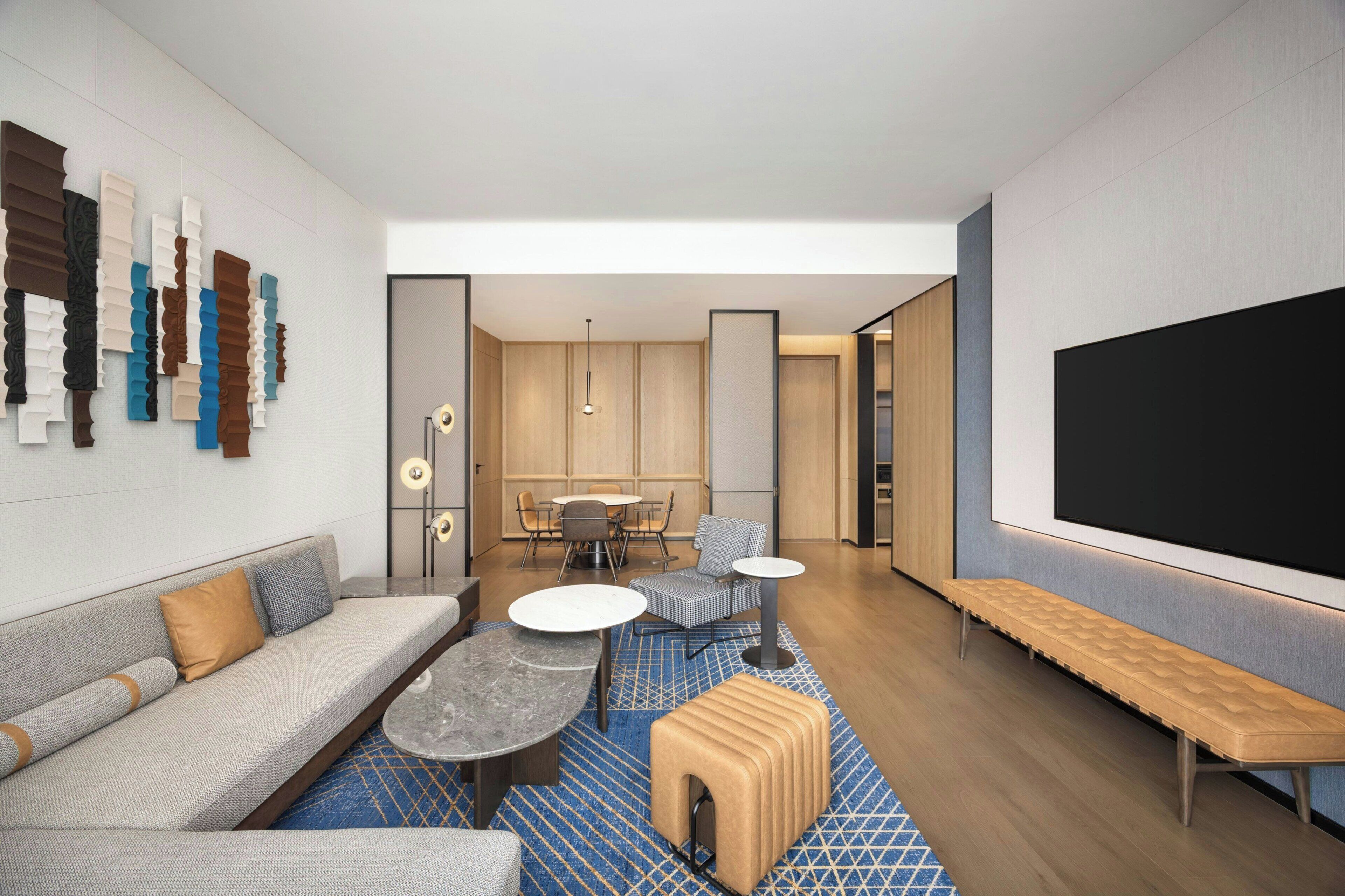 Un salon moderne avec un canapé, une table basse, un pouf et un grand téléviseur à écran plat.