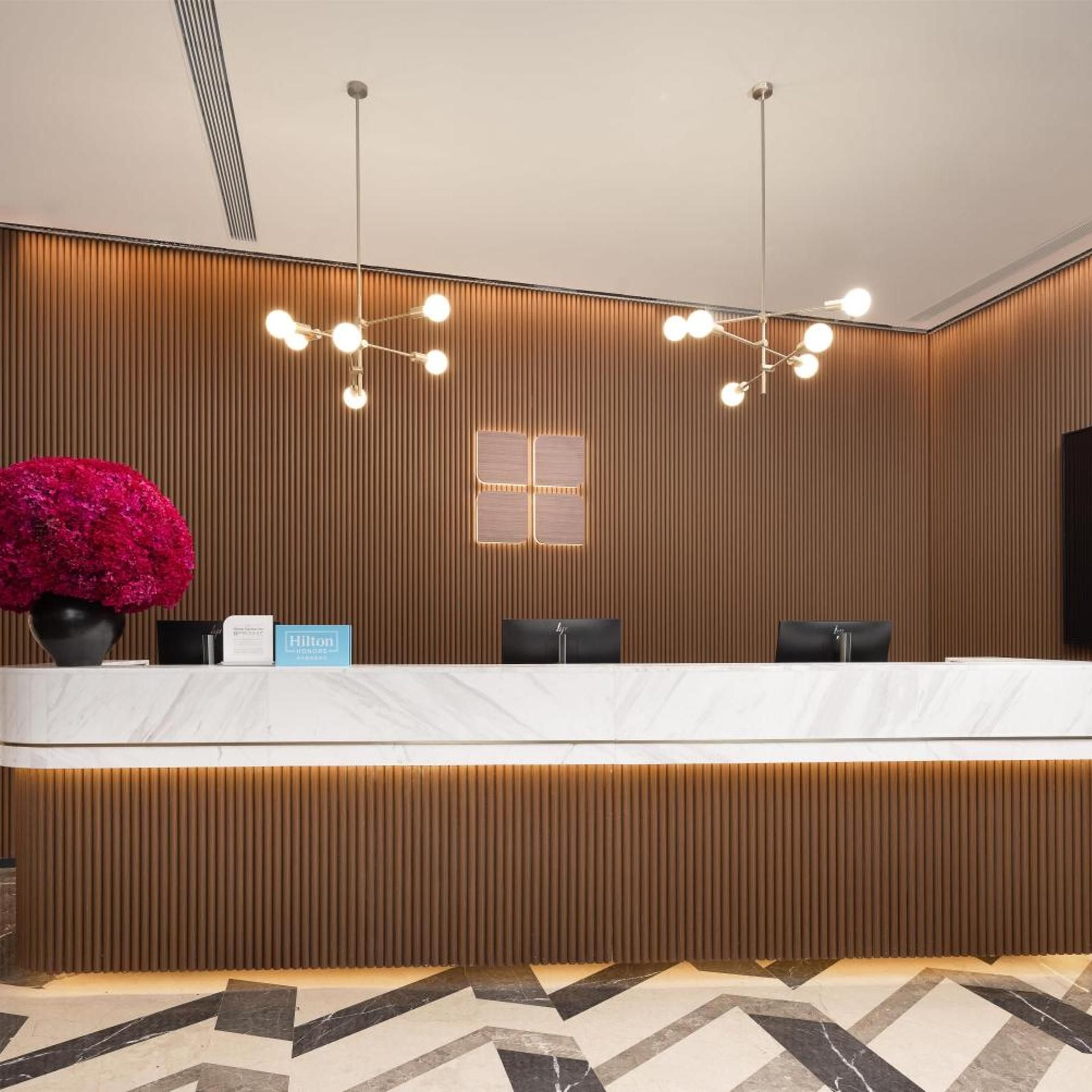 Una reception hotel dal design moderno, caratterizzata da un pannello decorativo in legno, un piano di lavoro in marmo e una grande pianta in vaso.