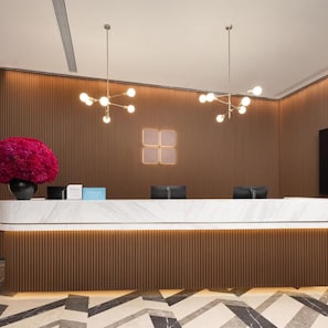 A hotel reception desk with a modern design, featuring a wooden panel wall, a marble countertop, and a large potted plant. - Hilton Garden Inn Chongqing Bishan (CHONGQING)