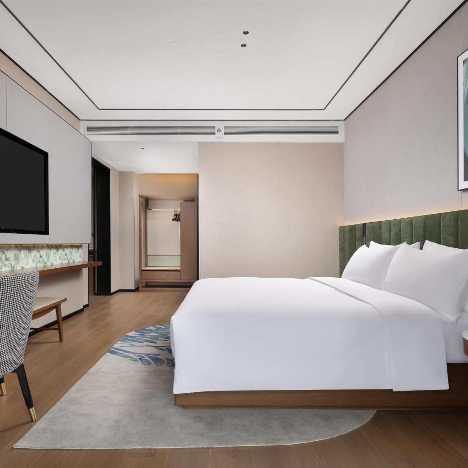Une chambre d’hôtel avec un grand lit, un téléviseur à écran plat, un bureau et un dressing.