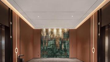 A modern elevator lobby with a marble floor and a textured wall.