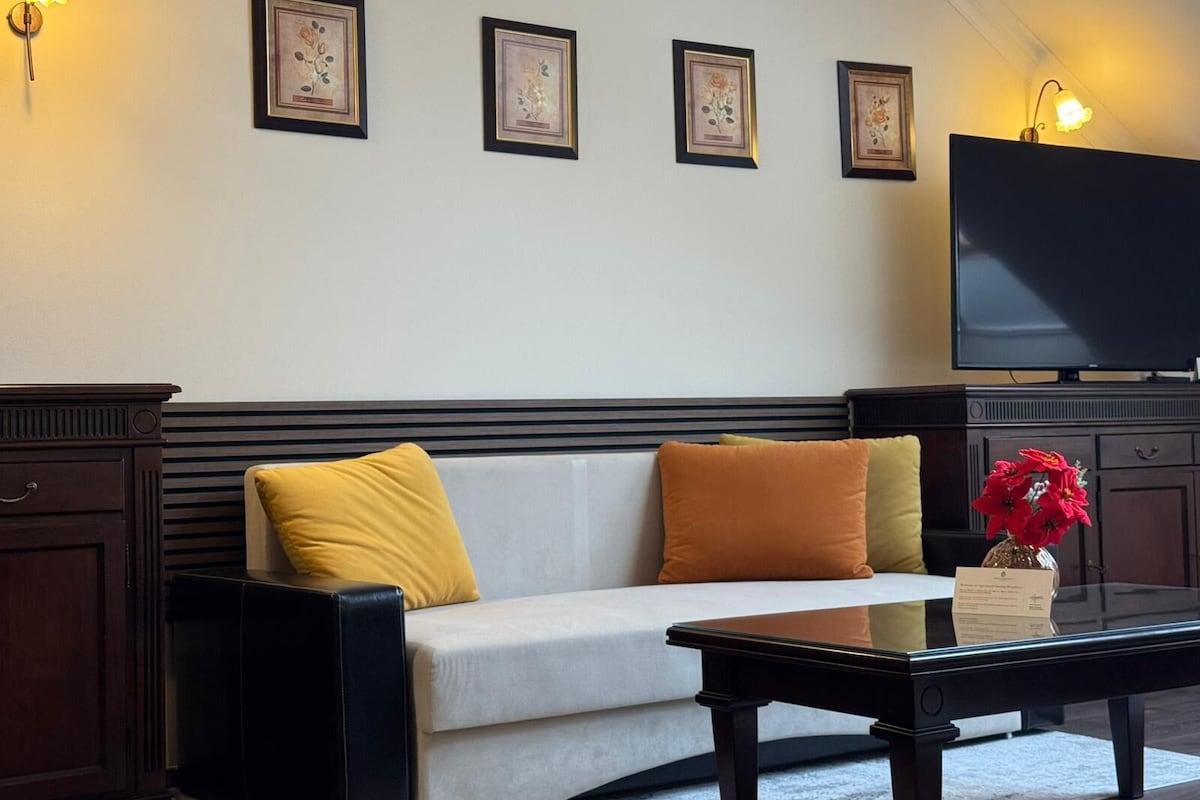 Una sala de estar con sofá, cojines, una mesita de centro y un televisor de pantalla plana.