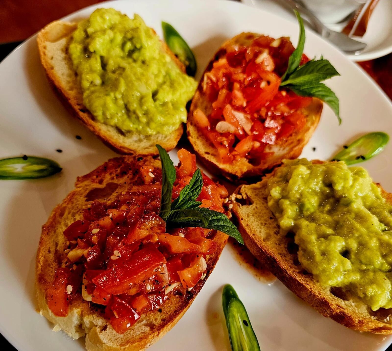 Four open-faced sandwiches with different toppings on a white plate.