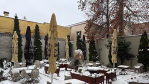 An outdoor seating area with tables and chairs covered in snow, surrounded by umbrellas and trees. - Hotel Iosefin Residence (Timișoara)