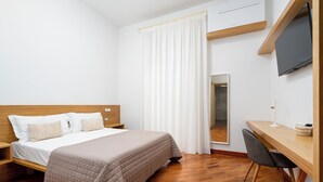 Ein Hotelzimmer mit Bett, Schreibtisch, Stuhl, Fernseher und Spiegel.