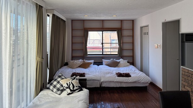 A hotel room with two beds, a large window with curtains, a built-in shelf, and a door. - Dream Terrace One Casa Dali (Tokyo)