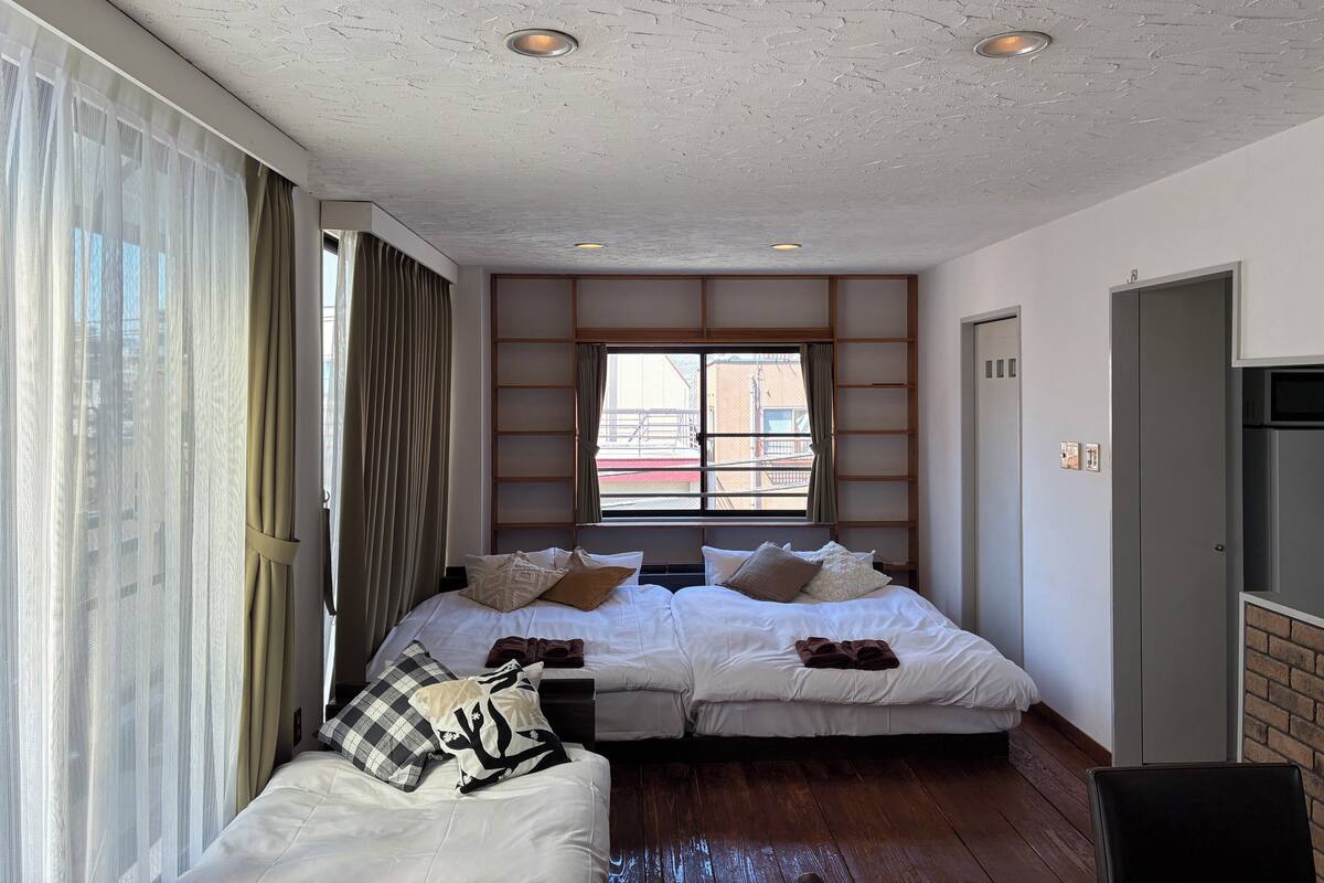 A hotel room with two beds, a large window with curtains, a built-in shelf, and a door.