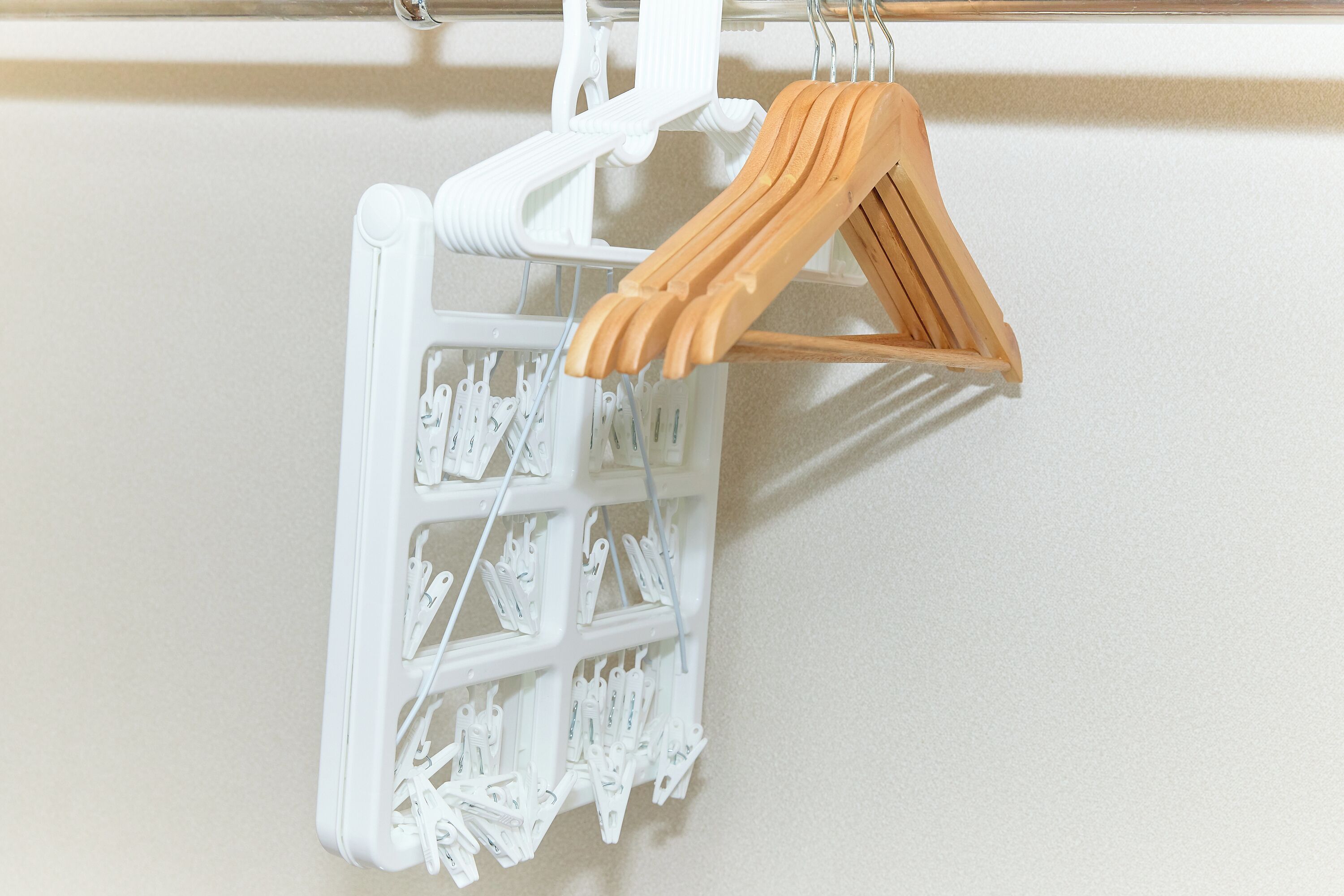 A white wall-mounted drying rack with wooden hangers and white plastic clips.