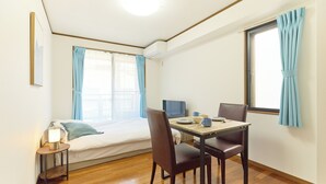A room with a bed, a table with chairs, a small bedside table with a lamp, and a window with curtains. - Dream Terrace One Casa Dali (Tokyo)