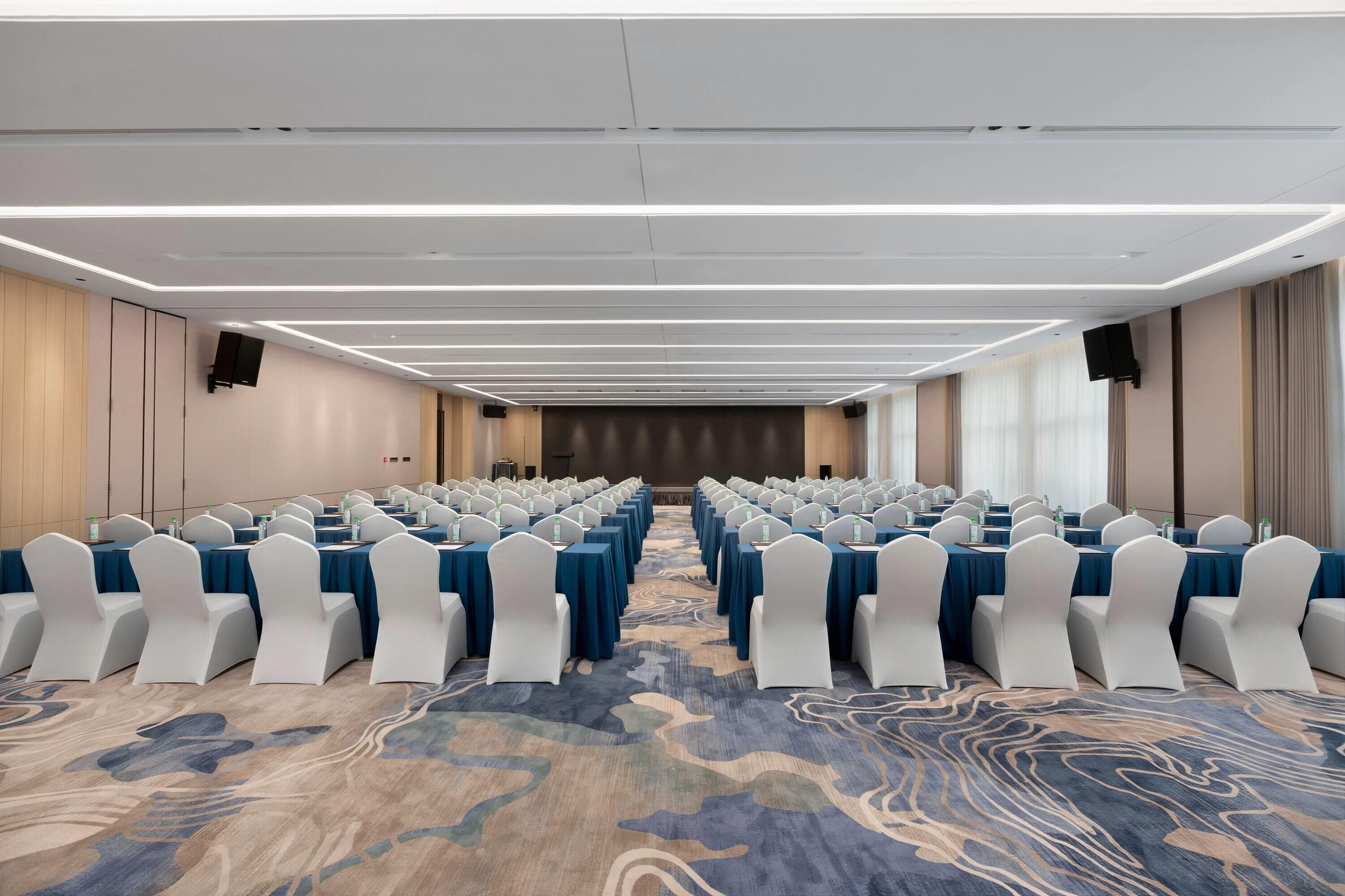 A conference room with rows of tables and chairs, a patterned carpet, and a modern ceiling design.