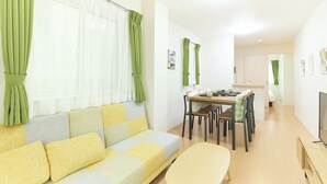 A living room with a sofa, a dining table with chairs, a television, and a kitchen area in the background. - Zenith Nakano Shinbashi (Tokyo)