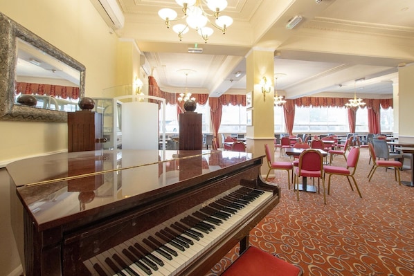 A grand piano in a hotel dining area with red upholstered chairs and a patterned carpet. - Bournemouth East Cliff by Belvilla - Superior Feature w/ View (Bournemouth)
