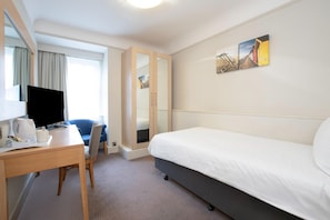 Quarto de hotel com cama, escrivaninha, computador, cadeira, espelho e obras de arte na parede.