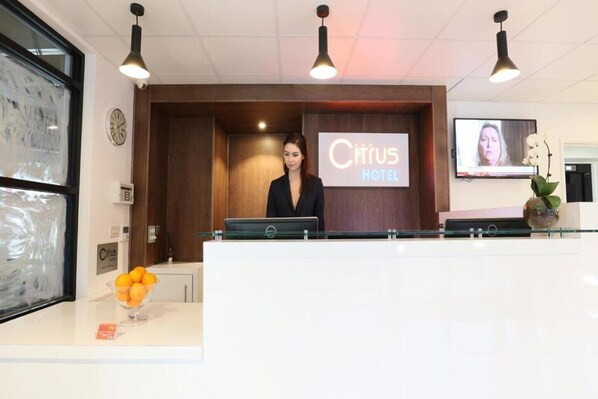 A hotel reception desk with a digital screen displaying the hotel's name, a clock, and a flower vase. - Standard Double Room (Cardiff)
