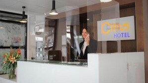 A hotel reception desk with a glass partition, a clock, and a sign for 'Citus Hotel'.