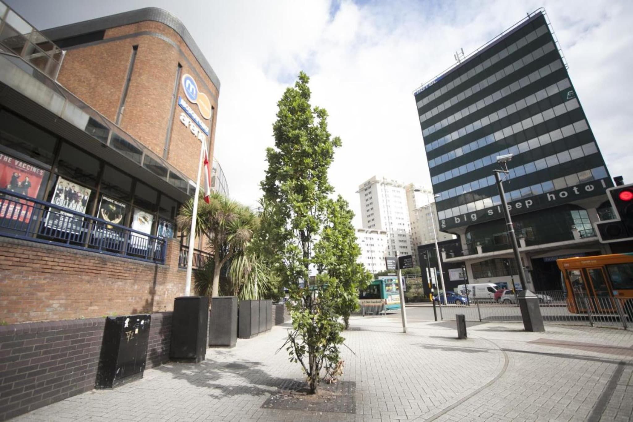 Una vista di strada con un edificio che presenta un'insegna per un hotel e un'altra per un'attività commerciale. C'è un albero al centro del marciapiede.