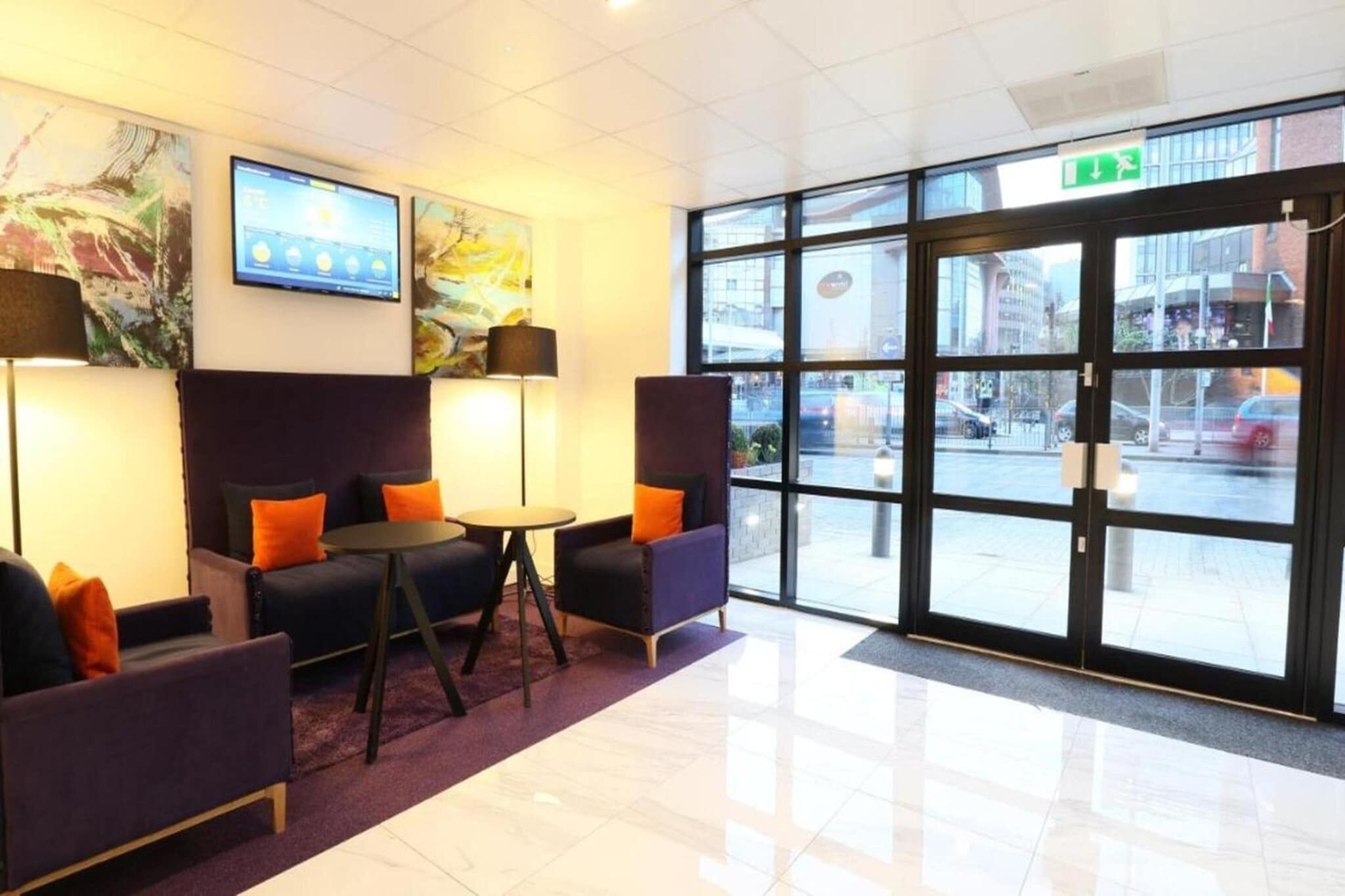 A lobby with seating, a digital display, artwork, and a view of the street.
