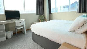 A hotel room with a bed, a desk with a chair, a television, and large windows.