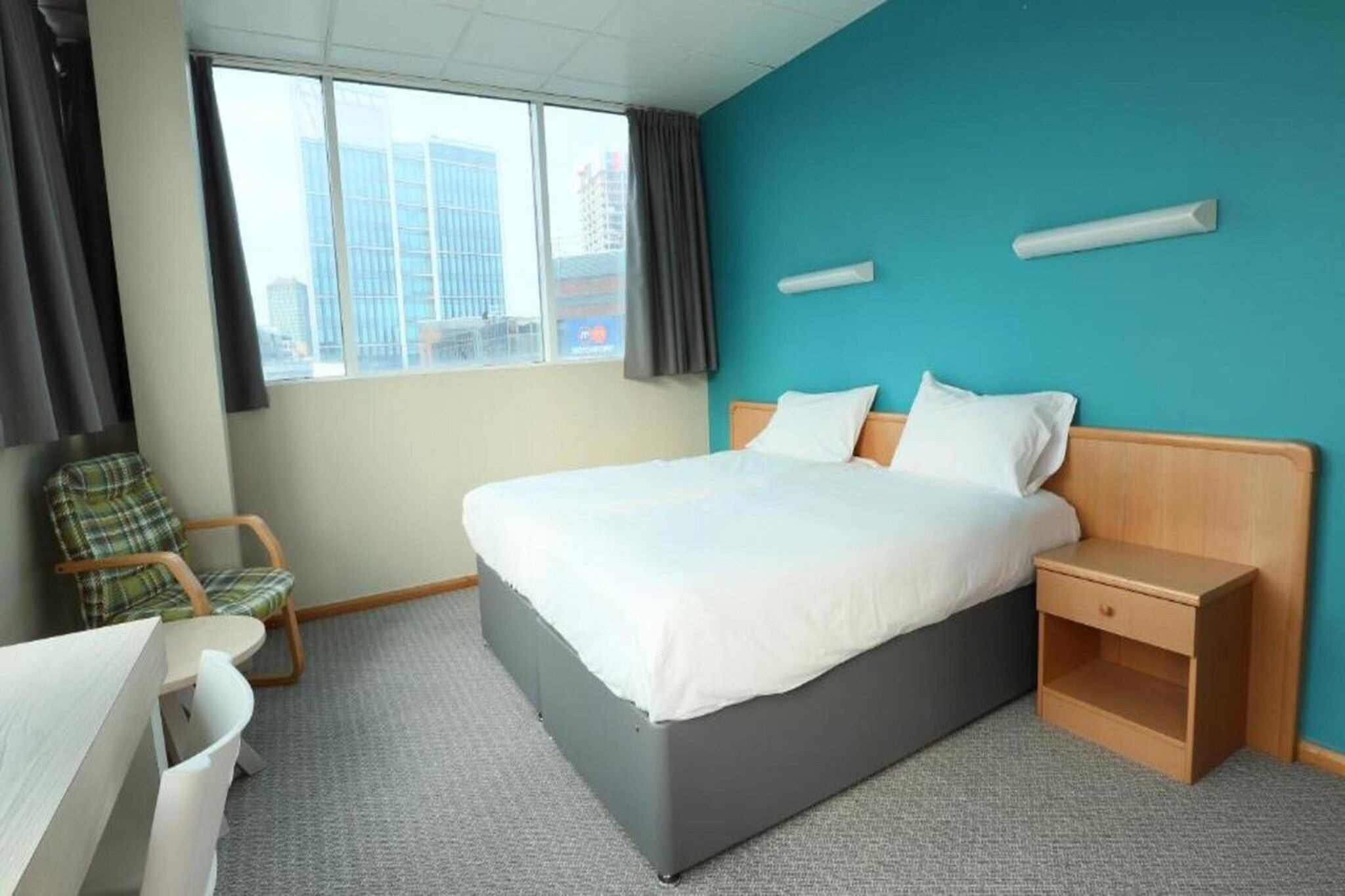 A hotel room with a bed, a desk, a chair, and a window with a city view.