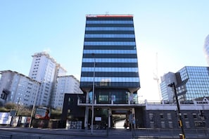 Un hôtel moderne avec une façade en verre, une entrée imposante et un drapeau sur le toit.