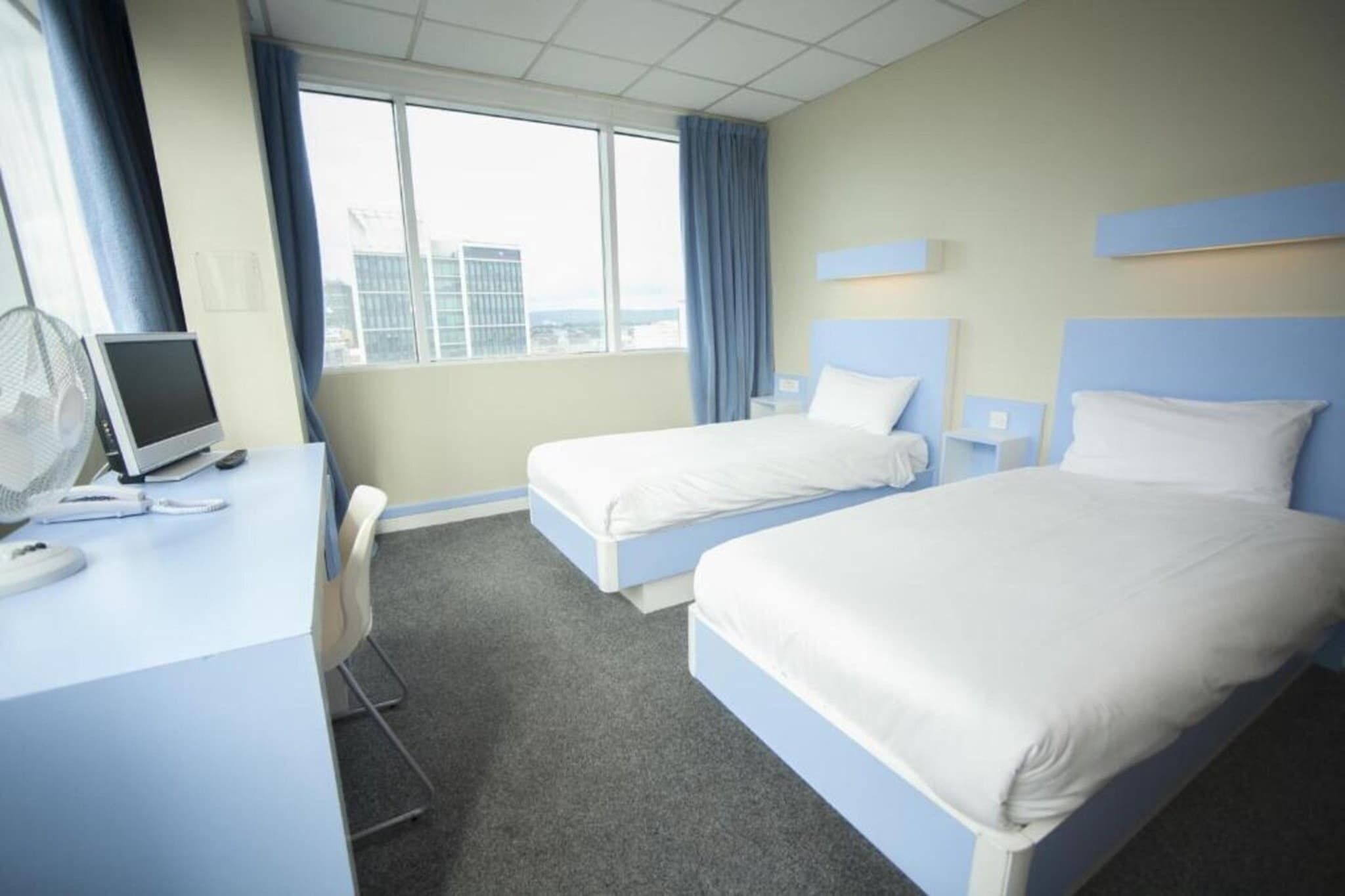 A hotel room with two beds, a desk with a computer, and a window with curtains.