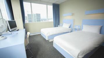 A hotel room with two beds, a desk with a computer, and a window with curtains.