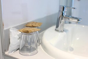 A bathroom with a white sink and a mirror. There are two clear glass bottles with brown paper labels on the sink. - Standard Triple Room (Cardiff)