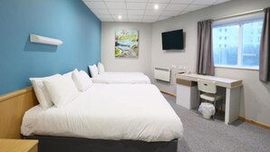 Habitación de hotel con dos camas, un escritorio, una silla, un televisor y una ventana con cortinas.